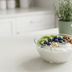 Bowl of plain Greek yogurt with berries, kiwi, oats, chia seeds, and walnuts beside an unbranded yogurt container.