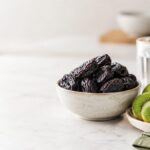 Prunes and sliced green kiwifruit arranged side by side for a comparison of foods used for constipation. Image Title: Prunes vs Kiwifruit for Constipation